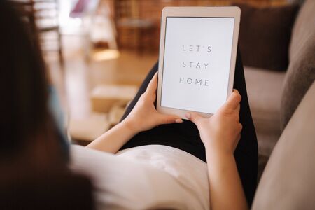 Mock up of woman in mask use tablet at home on sofa. Self isolated in quarantine. Stay Home Coronativus concept. COVID-19の写真素材