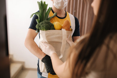 Delivery man in mask and gloves give fresh food to recipient and young woman customer. Stay home, Online shopping conceptの写真素材