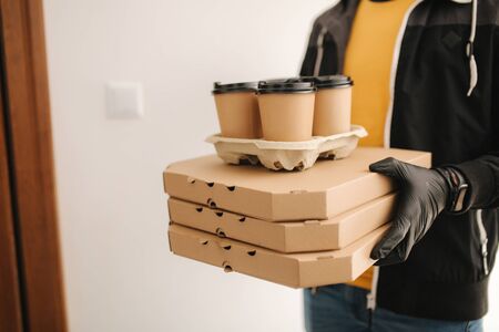 Close up of man hold tree boxes of pizza. Man delivery food and coffe to customer in mask and gloves. Coronavirus themeの写真素材