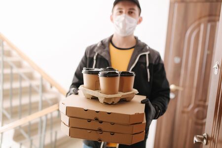 First persom view of delivery man in mask and gloves give pizza and coffe. Stay homeの写真素材