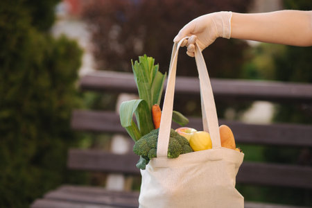 Female hand in medical gloves hold bag with fresh food, Vegetables, Fruits, Bread. After shop in...