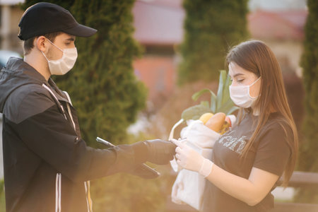 Smart food delivery service. Man in medical mask and gloves handing fresh food to young woman...