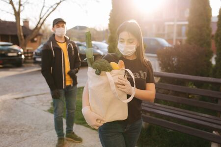 Courier in protective mask and medical gloves delivers fresh food for female customer. Delivery service under quarantine. Coronavirus covid-19 themeの写真素材