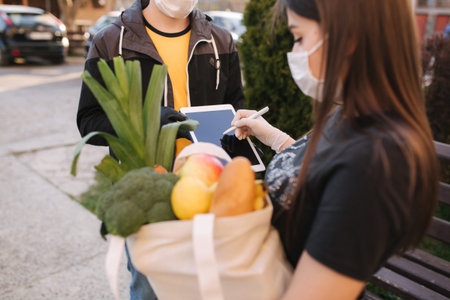 Smart food delivery service. Man in medical mask and gloves handing fresh food to young woman...