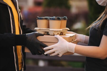 Closeup of courier give order to customer. Man from delivery service bring pizza and coffee. Hands in protective maskの写真素材