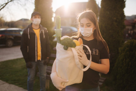 Courier in protective mask and medical gloves delivers fresh food for female customer. Delivery...