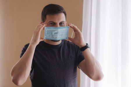 Man put on madical mask at home. Young man in protective mask. Coronavirus theme