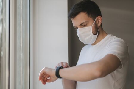 Young man in protective mask and look s out the window. Alone at home in quarantine. Coronavirus themeの写真素材