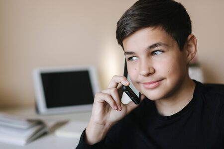 Portrait of young teenage boy at home speaking by phone. Background of tablet and booksの写真素材