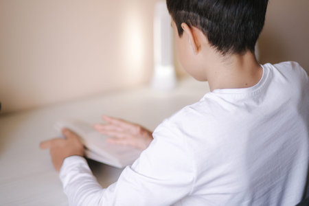 Young boy sitting at desk and read the book. Study at home during quarantine