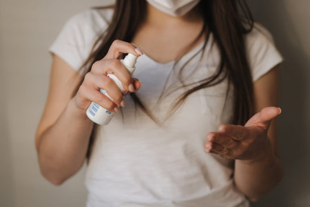 Young woman in white t-shirt and mask use sanitizerの写真素材