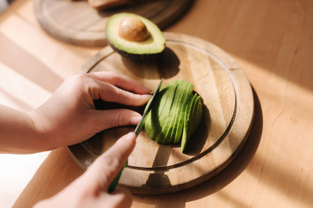 Close up of woman slicing avocado on wooden board at home. Vegetarian food concept