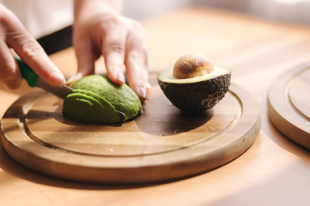 Close up of woman slicing avocado on wooden board at home. Vegetarian food concept.