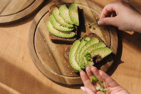 Avocado sandwich on dark rye bread made with fresh sliced avocados from above with sesame seeds and...