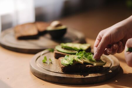 Avocado sandwich on dark rye bread made with fresh sliced avocados from above with sesame seeds and mustard seedlingsの写真素材