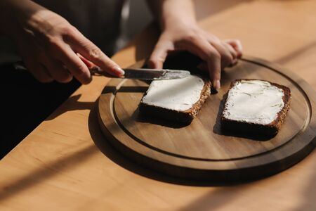 Close up of female butter the rye toasted bread by vegan butter. Woman butter toast at home on wooden boardの写真素材