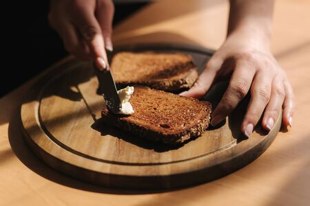 Close up of female butter the rye toasted bread by vegan butter. Woman butter toast at home on wooden boardの写真素材