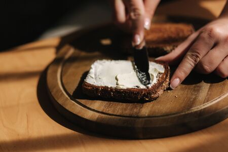 Close up of female butter the rye toasted bread by vegan butter. Woman butter toast at home on wooden boardの写真素材