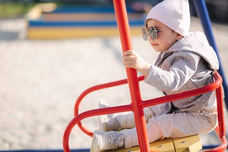 Adorable little girl on the swing set in playground. Happy little girl have fun. One and hulf year girlの写真素材