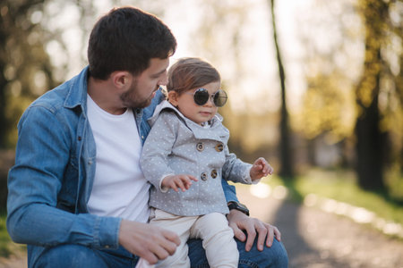 Cute daughter sitting on fathers lap. Portrait of dad and daughter in the park