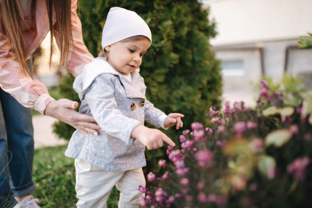 Adorable little girl with mom smels pink flowers from flowering tree. Happy family