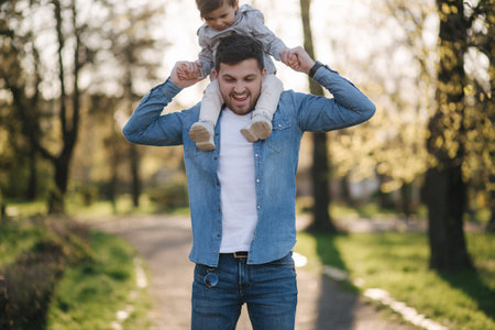 Adorable little daughter sitting on dads neck and laughing. Young father walk with his cute daughter...