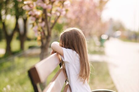 Happy female kid sits on the bench in the park. Fresh air. End of quarantineの写真素材