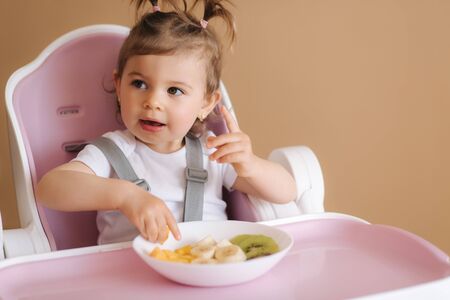 Portrait of happy young baby girl in high chair eating exotic fruitsの写真素材