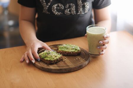 Close up of woman hold toast with guacamone in one hand and smoothie in another. Vegan lunchの写真素材