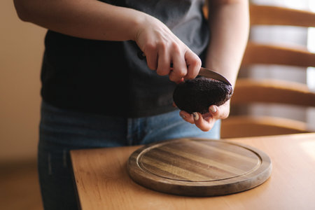 Close up of woman slicing avocado on wooden board at home. Vegetarian food concept