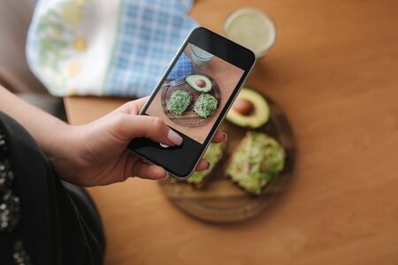 Woman make photo of lunch at home. Female glogger make food photography. Healthy vegan food. Toast with avocado and smoothie with spinachの写真素材