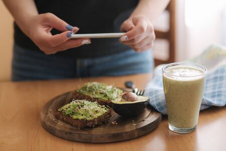 Woman make photo of lunch at home. Female glogger make food photography. Healthy vegan food. Toast with avocado and smoothie with spinachの写真素材