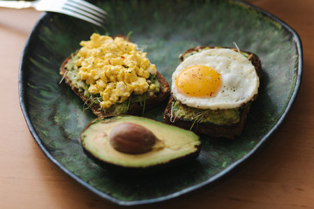 Different cooked egg on avocado sandwich with whole grain bread on green plate. Smoothie with...