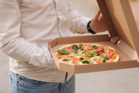 Middle selection of young man opening pizza box outdoors. Fresh vegetarian pizza, basil, tomatoes, broccoli and lactose free cheeseの写真素材