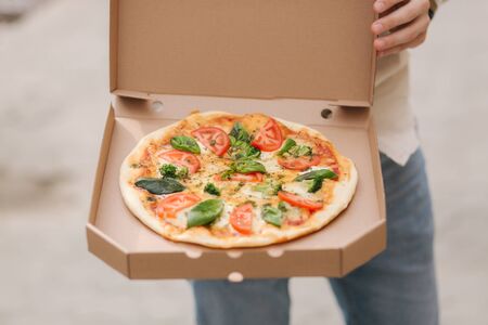 Middle selection of young man opening pizza box outdoors. Fresh vegetarian pizza, basil, tomatoes, broccoli and lactose free cheeseの写真素材