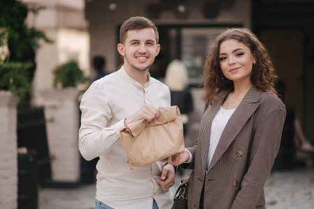 Young couple hold takeaway food in hands and smile to camera. Space for text