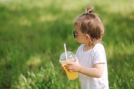 Close-up of cute little girl in white bodysuit and sunglasses drink lemonade outdoorsの写真素材
