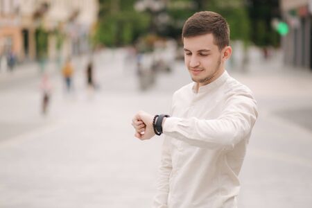Man looking at the watch outdoors. Young man in white shirt in the cityの写真素材