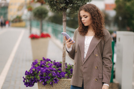 Attractive young woman with curly hair use phone in city. Happy beautiful woman writing massage on...