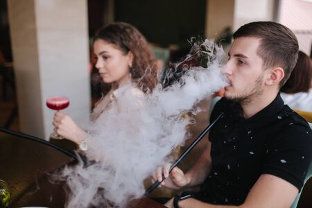 Group of people smoke hookah on terrace. Man and women meet in restaurantの写真素材