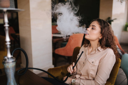 Attractive young woman smoke hookah in restaurant. Woman with hookah on terrace by herself