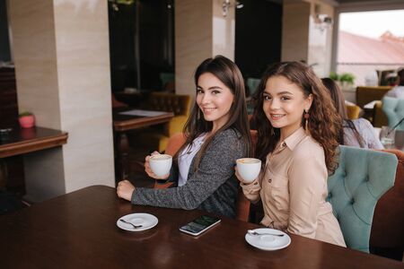 Two female friends drink coffe in restauratn and speak. Beautiful women metting in cafe. End of quarantineの写真素材