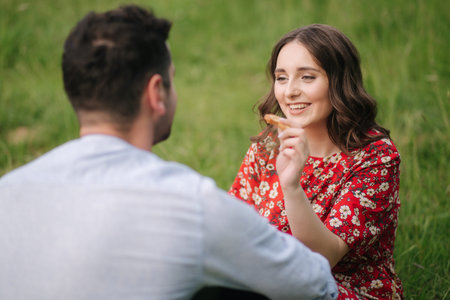 Happy couple spend time outdoors on mini picnic. Attractive woman and handsome man sits on red...