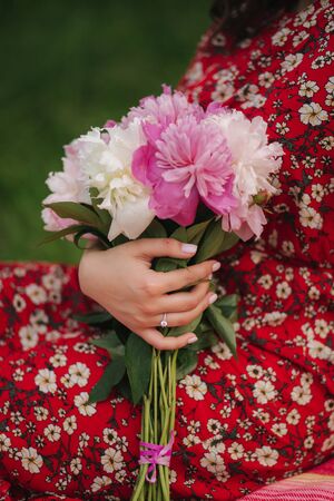 Close up of woman with engagement ring hold bouquet of peony flowersの写真素材