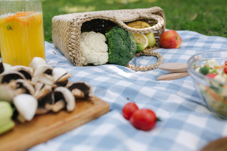 Picnic basket with healthy vegan sandwiches on blue checkered blanket in park. Fresh fruits,...