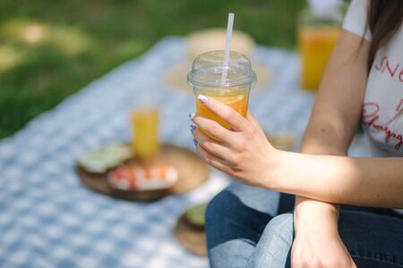 Close-up of woman hold disposable cup with orange lemonade on picnic outdoors. Space for textの写真素材