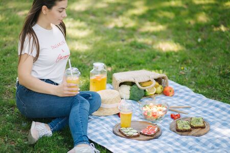 Woman hold disposable cup with orange lemonade on picnic outdoors. Space for text. Vegan picnic conceptの写真素材