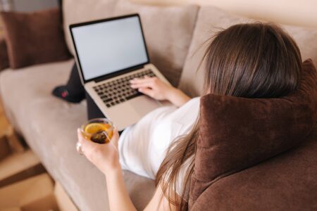 Woman shopping online at home use tablet. Woman work on tablet and drink tea. Quarantine time. Boxes on the floor. Parcelの写真素材