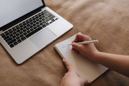 Top view of woman on the bed using laptop and writing down in notebook. Covid-19の写真素材