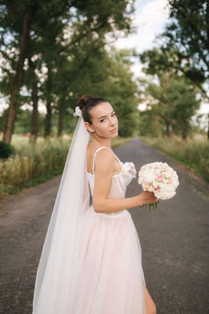 Gorgeous bride in elegant wedding dress stand in linden alley with bouquet and posing to photographerの写真素材